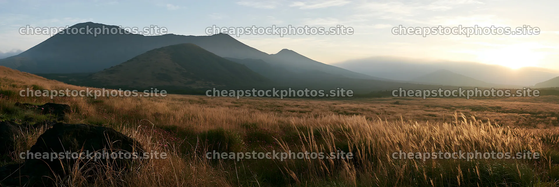 Kumamoto volcanic meadow dark rock foreground at sunrise – stock photos 13690x4602