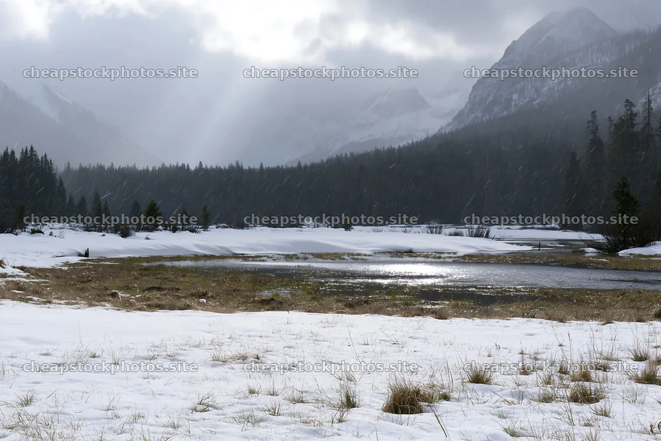 Snowbound meadow with river under cloudy skies – stock photos 9722x6480